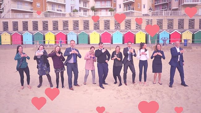 A group of happy employees on Bournemouth beach with brightly colored beach huts behind them